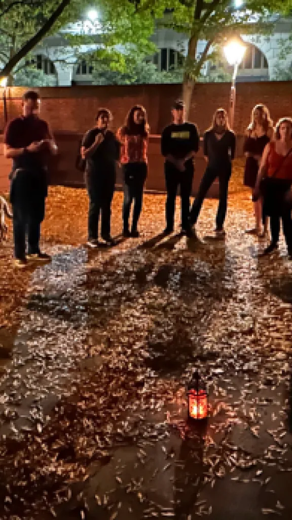 A Ghost Tour of Philadelphia tour group stands around a tour guide with a lantern in a leaf-strewn courtyard