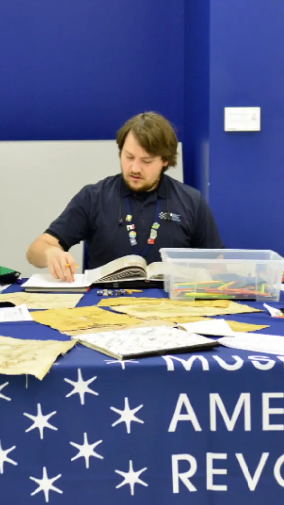 Three children do a craft with a Museum of the American Revolution employee at a History Explorer Day Camp