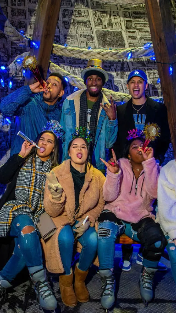 Group of 7 mixed gender/race people posing smiling, laughing and celebrating New Year's with party favors. 