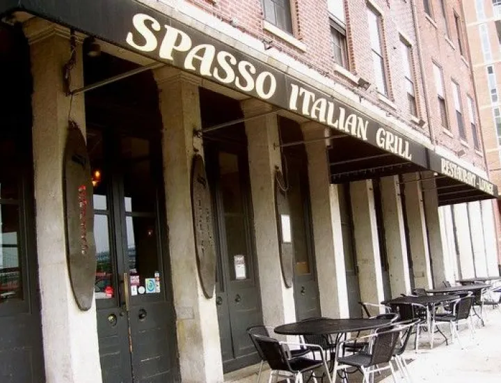 Exterior of Spasso Italian Grill showing front door, outdoor seating, and black awning with restaurant name printed in white