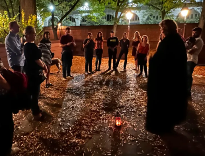 A Ghost Tour of Philadelphia tour group stands around a tour guide with a lantern in a leaf-strewn courtyard