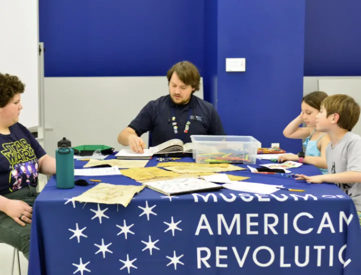 Three children do a craft with a Museum of the American Revolution employee at a History Explorer Day Camp