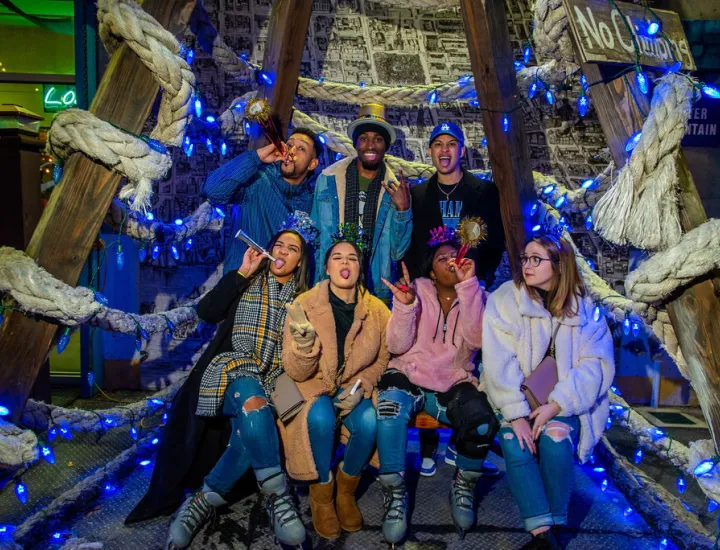 Group of 7 mixed gender/race people posing smiling, laughing and celebrating New Year's with party favors. 